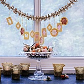 Christmas biscuits hanging from garland above dish of decorations on window sill