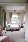 Feminines Schlafzimmer in sanften Rosetönen mit altem weißem Kleiderschrank und Doppelbett mit gepolstertem Fussende. Geraffte, verspielte, helle Vorhänge im Hintergrund des eleganten Landhausambiente.