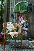 Wicker chair decorated with green beads and floral cushions on patterned rug; colourful postcards and memorabilia on old barn wall