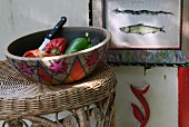 Colourful ceramic bowl of vegetables on wicker stool; framed picture of fish on wall