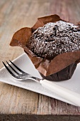 A chocolate muffin dusted with icing sugar in a paper case
