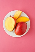 Frische Mango, ganz & aufgeschnitten auf Teller (Aufsicht)