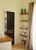 Corner of modern kitchen - fitted fridge-freezer with blackboards on doors next to crockery on shelves