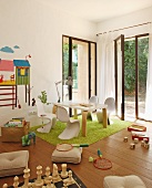 Modernes Kinderzimmer mit weissen Schalenstühlen und Tisch auf grünem Teppich vor offener Terrassentür