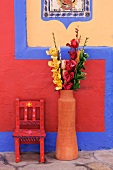 Farbenfrohe Wandgestaltung; davor eine Terrakottavase mit Kunstrosen und ein bemalter Kinderstuhl
