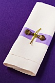 weiße Leinenserviette mit Serviettendeko auf einer violetten Leinentischdecke