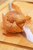 A onion and a knife on a wooden chopping board