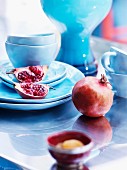 Pomegranates and pastel blue china crockery on shiny table top