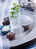 Sprig of peppermint in glass of water, sugar bowl and wooden printing blocks on metal dish