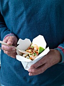 A man holding a take-away box of prawn salad