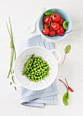 Freshly shelled peas in a colander and vine tomatoes in a bowl