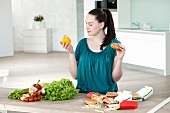 Junge Frau mit Fast Food und mit frischem Gemüse in der Küche