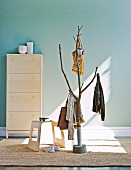 Pattern of light and shade on stylised tree as coat rack and modern stool in front of shoe cabinet against pastel blue wall