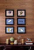 Künstlerische Objekte im Bilderrahmen an Holzwand über Sideboard mit diversen Dekowaren