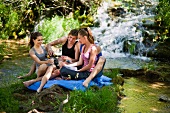 Young people sitting on a picnic rung in front of a waterfall with champagne
