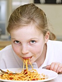 Mädchen isst Spaghetti mit Tomaten