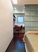 Bed with satin linen in front of an upholstered room divider and view of an antique chair by a window