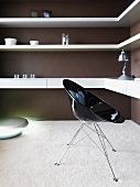 Black shell chair in front of wall mounted shelving on a brown wall in a living room corner