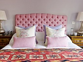 Double bed with scatter cushions against headboard with pink upholstery