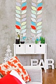 Kissen auf Sofa und weisses Wandtisch vor grauer Wand in Betonlook mit aufgeklebten Blattmotiven