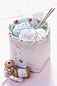 Balls of wool and knitting needles in pink basket next to vintage reels of yarn