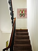Blick über Treppe mit braunem Teppichbelag und schmiedeeisernem Geländer auf Bild mit Schuhmotiv an Wand in traditionellem Treppenhaus