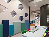 Ein Spieltisch mit bunten Stühlchen vor einer Wand mit vieleckigen Öffnungen im modernen Kindergarten