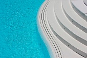 Eine weiße, abgerundete Treppe führt zum Pool mit geschwungenem Rand
