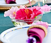 A place setting and a bowl of water hibiscus flowers