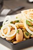 A white broad bean salad with olives and onions served with pita bread