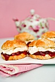 Scones with strawberry jam and cream with a pot of tea in the background