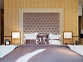 Doppelbett mit modernen Lampen und gepolstertem Kopfteil in Raumteilerwand zum Bad Ensuite