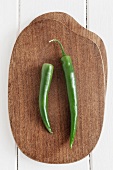 Two green chilli peppers on a chopping board