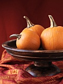 Three orange pumpkins in wooden bowl