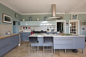 Moderne, große Küche mit blau-grauen Schrankfronten und Barhocker vor freistehendem Küchenblock in ländlichem Ambiente