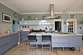 Large, modern kitchen with blue-grey cupboard doors and bar stools at free-standing kitchen island in country-style atmosphere