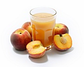 A glass of peach juice surrounded by whole and halved peaches