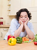 Frau schaut gelangweilt auf Gemüse in der Küche