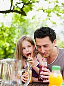 Vater und Tochter trinken Fruchtsäfte im Garten