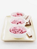 Three small bowls with cherry ice cream and ice cream wafers on a serving tray
