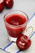 A glass of cherry juice with a fresh cherry