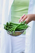 A young woman holding a colander of green beans