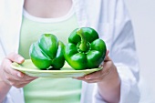 A young woman holding two green peppers on a plate