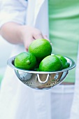 A girl holding a colander of limes