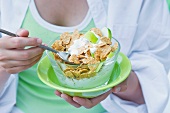 A girl eating cornflakes with yogurt and apple