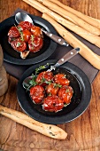 Confit tomatoes in olive oil with lemon thyme and balsamic vinegar and olive bread sticks on a wooden board