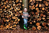 A little boy standing in front of a stack of wood