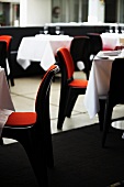 Gedeckte Tische, dazu Stühle mit orangefarbenen Sitzpolstern in einem Restaurant