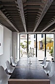 Transparent glass candelabra and white Eames chairs at a contemporary dining table in a living room with a bank of windows to the terrace and a unique steel and wood ceiling