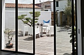 View through a bank of windows onto a terrace with a small topiary tree and modern patio furniture